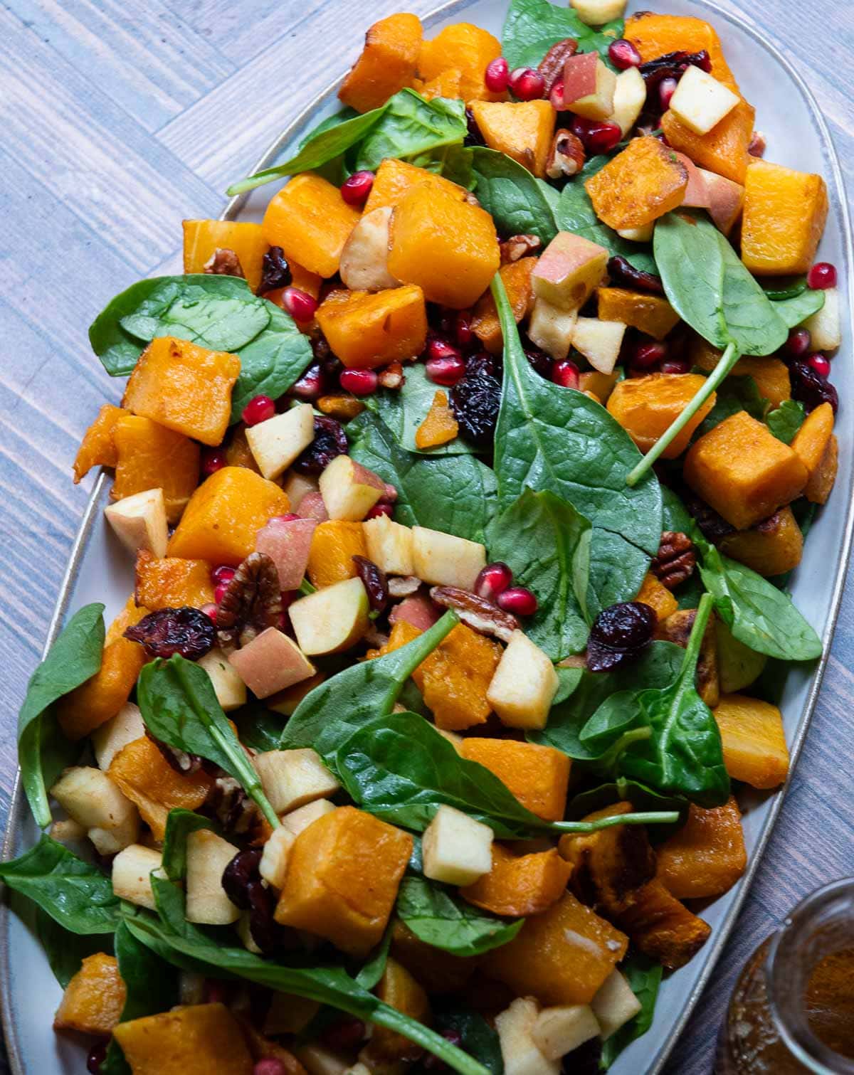 Roasted butternut squash salad with apples, pecans, spinach, cranberries on a platter along with the apple cider vingegar dressing.